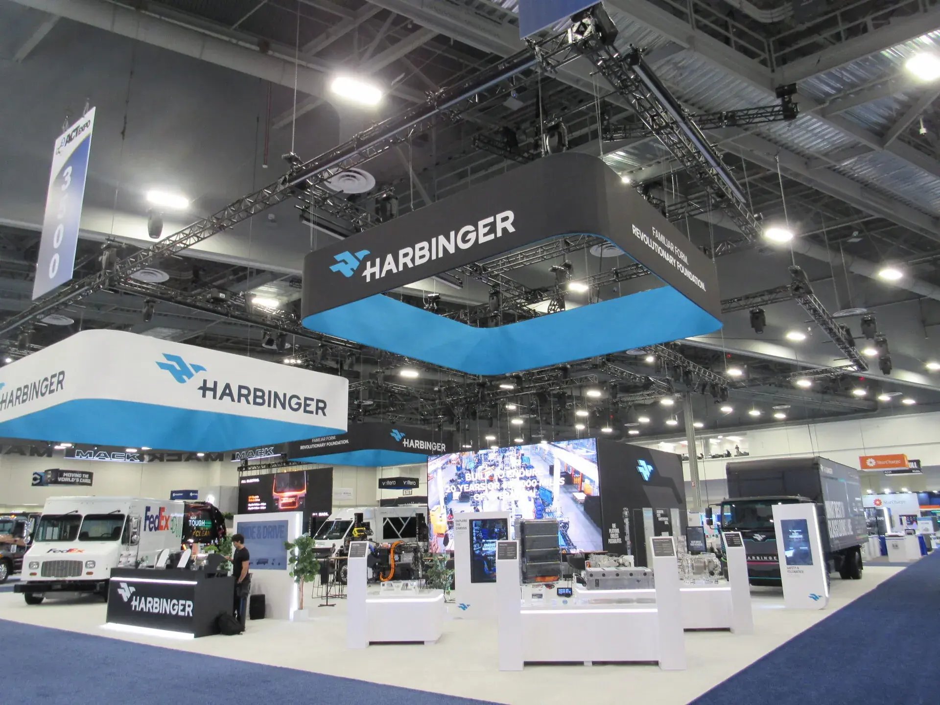 Harbinger ACT Expo booth overview with hanging sign, LED wall, and electric truck display