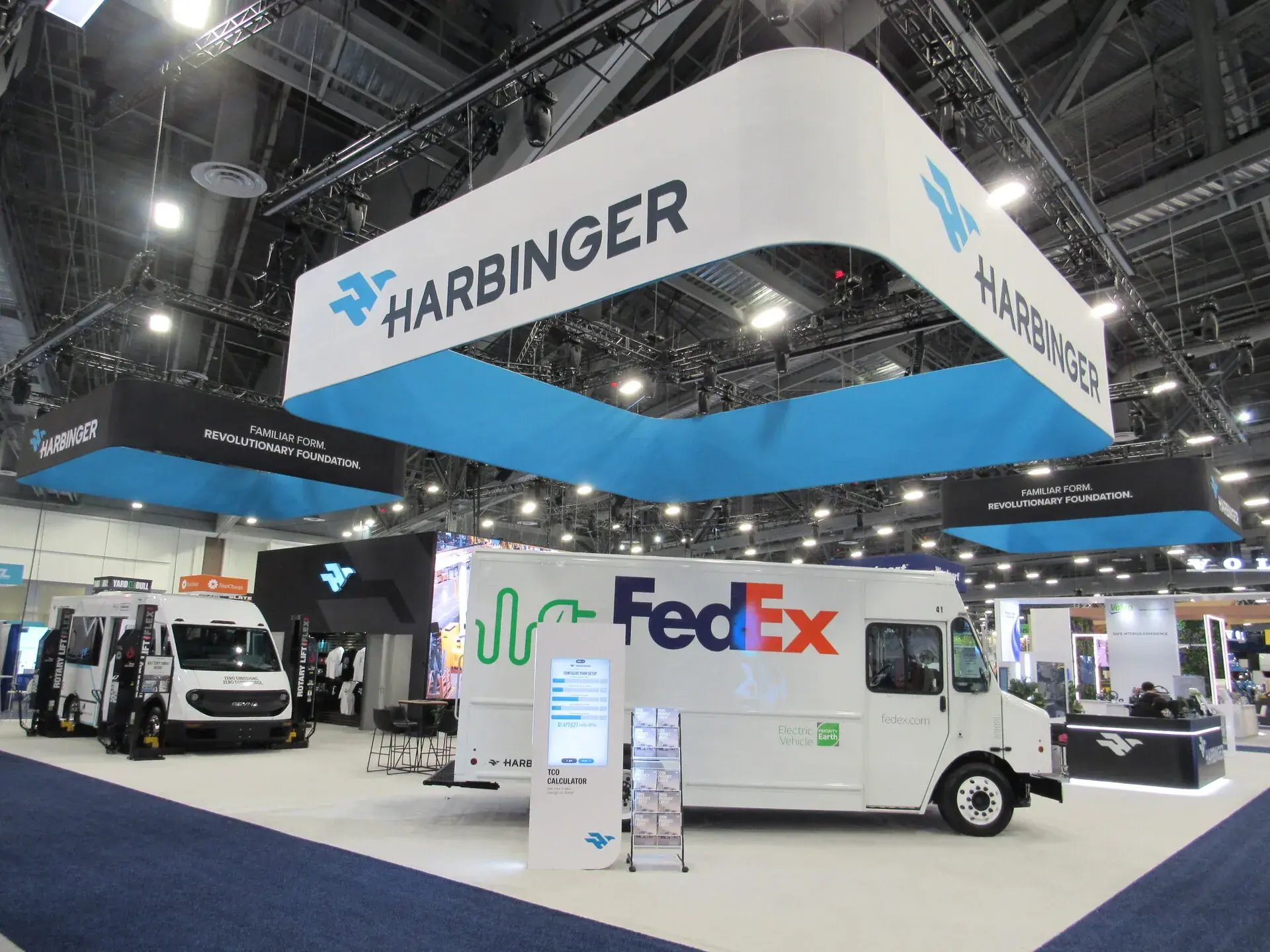Harbinger 80x80 island exhibit at ACT Expo with oversized hanging sign and blue brand lighting
