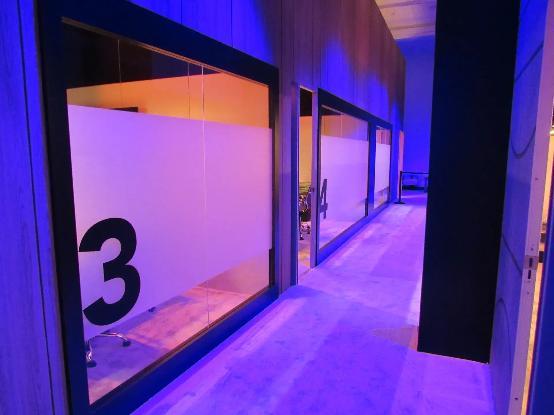 Accent-lit corridor with numbered private meeting rooms showing theatrical lighting design