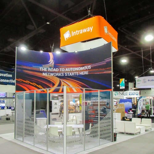 Intraway trade show booth with glass walls for private meeting room and large orange overhanging sign with logo