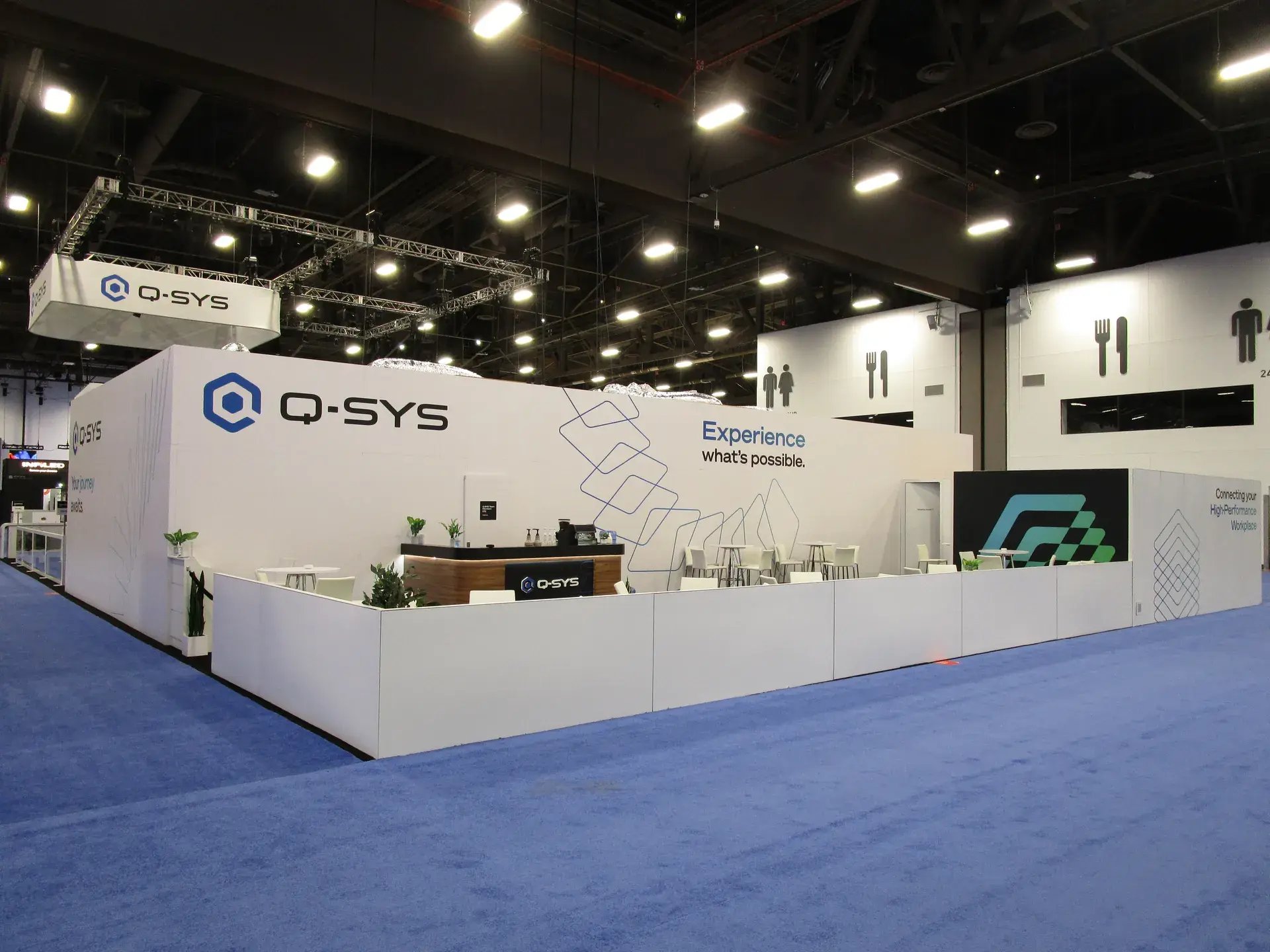 Q-SYS 60x90 island exhibit at InfoComm with illuminated logo wall and overhead hanging sign