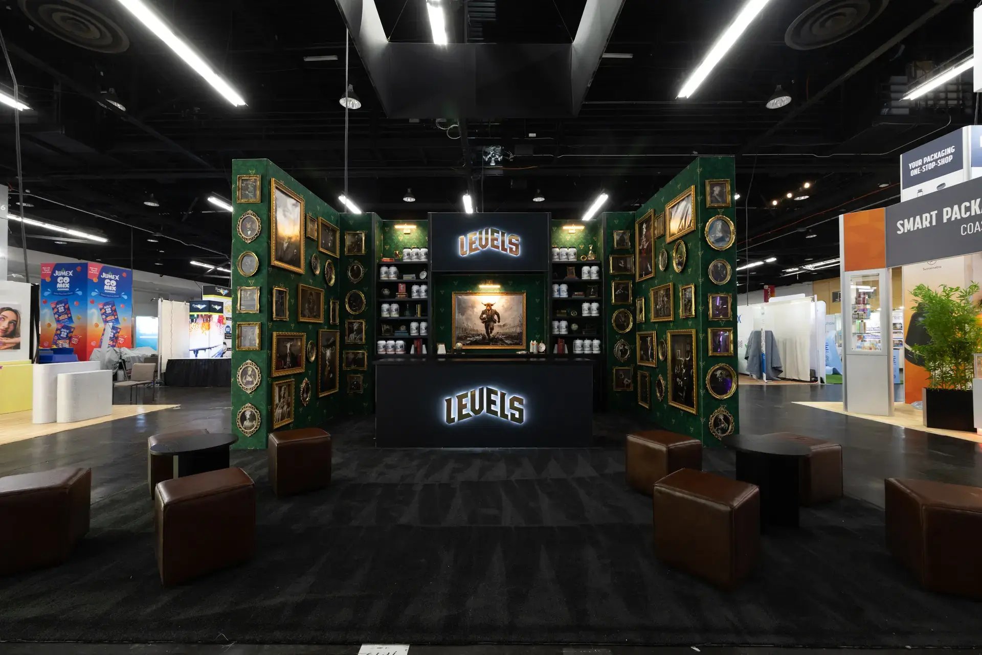 Front view of the LEVELS exhibit with leather ottomans and side tables on black carpet facing the illuminated front counter