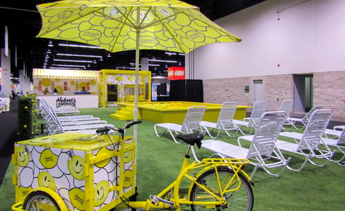 Hubert's Lemonade trade show booth with a ball pit pool and lawn chairs and a bike with a umbrella serving lemonade